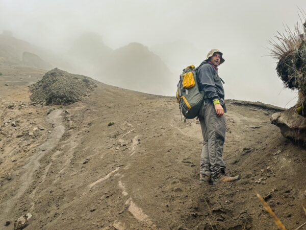 Hiker with a backpack navigating a misty, rocky slope near Volcán Ruminahui, Ecuador, surrounded by fog and gray terrain.