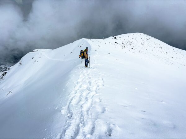 Climbers trek across the snow-covered summit of Chimborazo Volcano in Ecuador, surrounded by misty clouds.