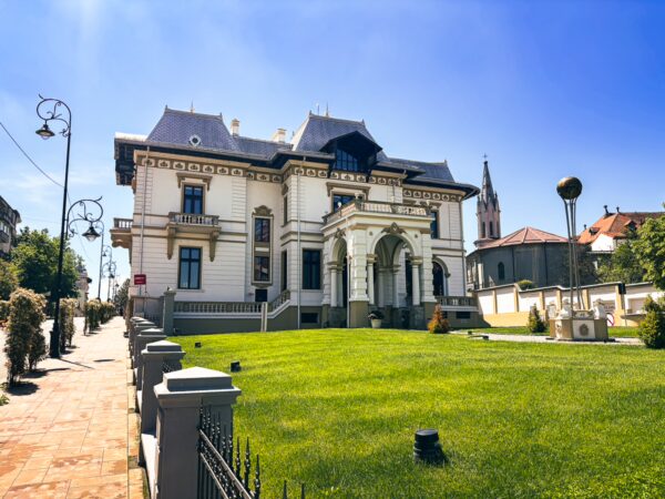 Elegant architecture and lush lawns surround a historic villa in Craiova, Romania, under a clear blue sky.