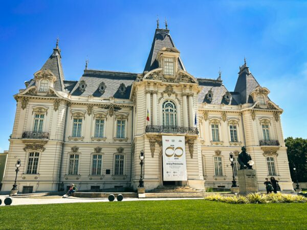 Art museum with ornate architecture and a bright blue sky in Craiova, Romania, showcasing intricate details and manicured lawns.