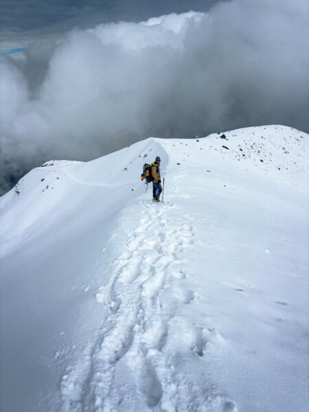 Majestic Chimborazo Volcano features a climber navigating a snowy ridge with clouds swirling below, showcasing Ecuador's stunning landscape.