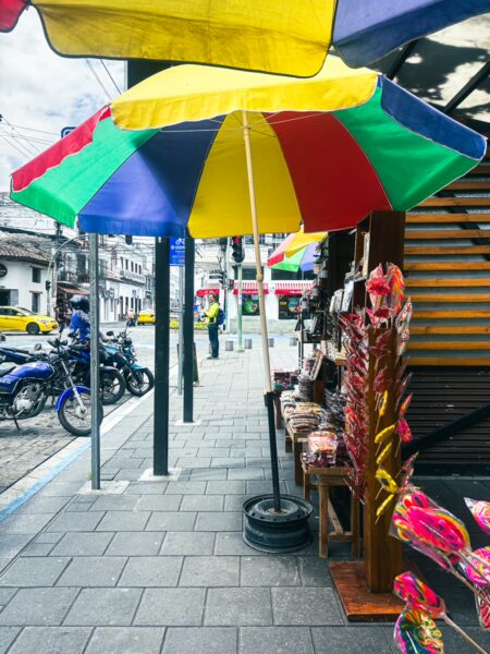 Colorful umbrellas shade a vibrant street market in Ibarra, Ecuador, showcasing local crafts and bustling activity.
