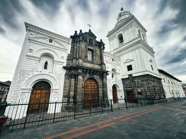 San Agustin Church features stunning white and stone architecture under a dramatic sky, showcasing Quito's historic charm.