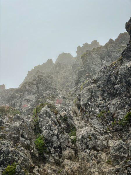 Majestic rocky slopes of Imbabura Volcano shrouded in mist, showcasing rugged textures and lush green patches in Ecuador.