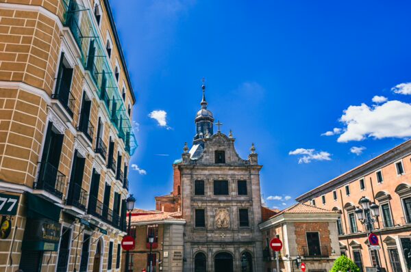 Charming streets of Madrid showcase historic architecture with a striking bell tower under a vibrant blue sky.