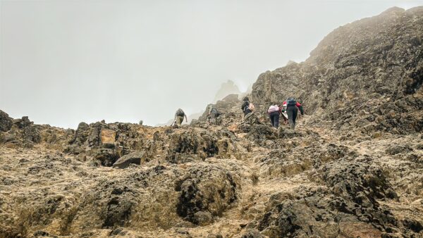 Hikers ascend the rocky terrain of Pichincha Volcano, surrounded by mist and rugged mountain peaks in Ecuador.