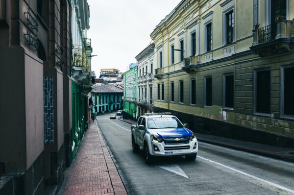 White and blue vehicle drives along a narrow street flanked by colorful colonial buildings in Guayaquil, Ecuador.
