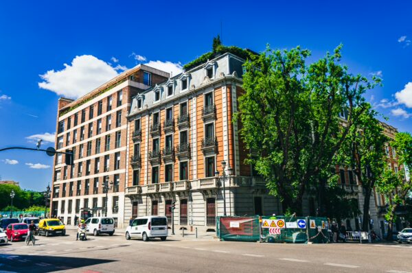 Elegant buildings line the street in Madrid, Spain, showcasing rich architecture under a bright blue sky with fluffy clouds.
