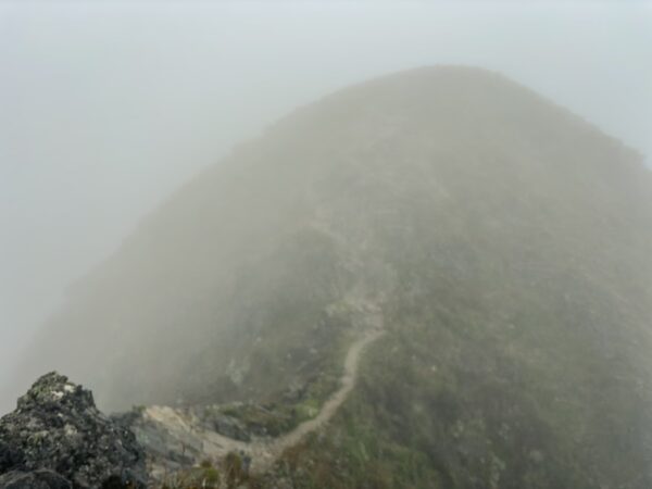 Misty slopes of Imbabura Volcano in Ecuador, with a winding path disappearing into the clouds and rocky terrain.