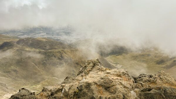 Majestic Rucu Pichincha Volcano rises amid wispy clouds, showcasing rocky terrain and green hills of Ecuador below.