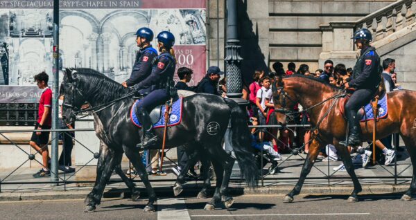 Calle de Bailén features police officers on horseback, surrounded by a lively crowd against a backdrop of historic architecture in Madrid.