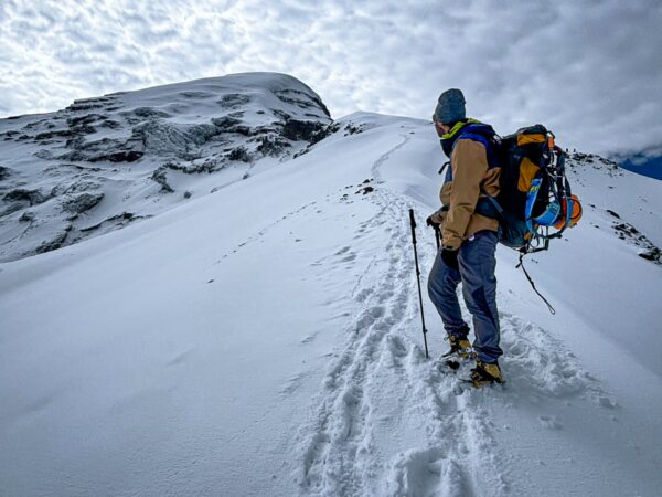 Climber ascending the snowy slopes of Chimborazo Volcano in Ecuador, surrounded by a cloudy sky and snow-covered terrain.