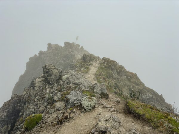 Jagged rocky peak shrouded in mist, leading to Imbabura Volcano in Ecuador, highlighting the rugged terrain and overcast sky.