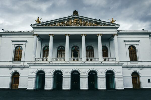 Teatro Sucre in Quito features neoclassical architecture with grand columns and intricate golden details against a cloudy sky.