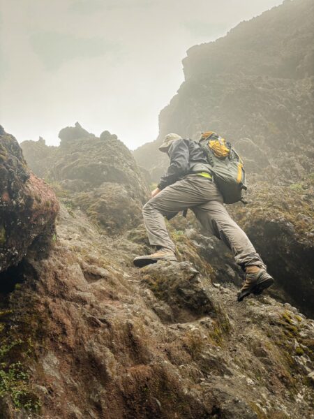 Climber ascending rocky terrain with misty backdrop at Volcán Ruminahui, Ecuador, showcasing rugged landscape and atmospheric conditions.