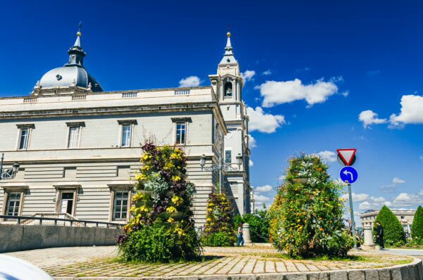 Catedral de Santa María in Madrid showcases beautiful architectural details against a vibrant blue sky, surrounded by green landscaping.