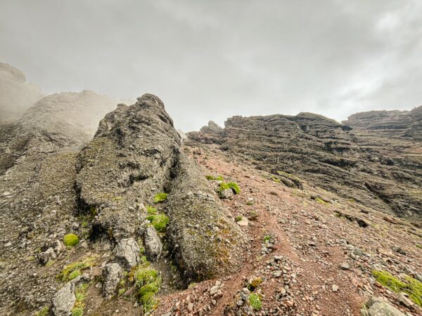 Stony terrain with rugged cliffs and sparse green vegetation beneath a cloudy sky at Volcán Ruminahui, Ecuador.