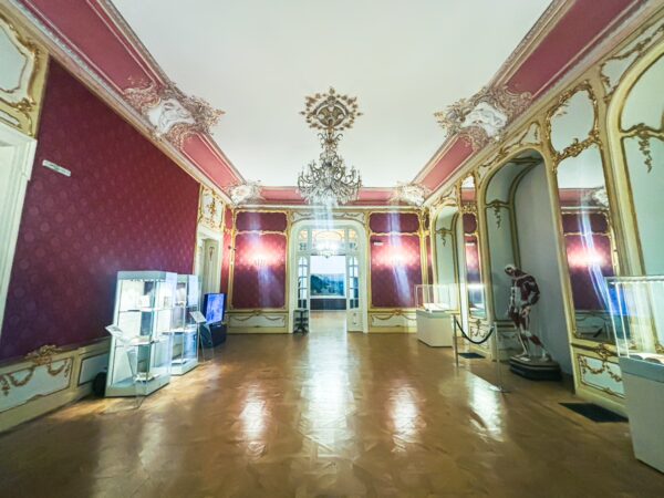 Elegant interior of the Craiova Art Museum, featuring ornate red walls, a chandelier, and displayed artworks.