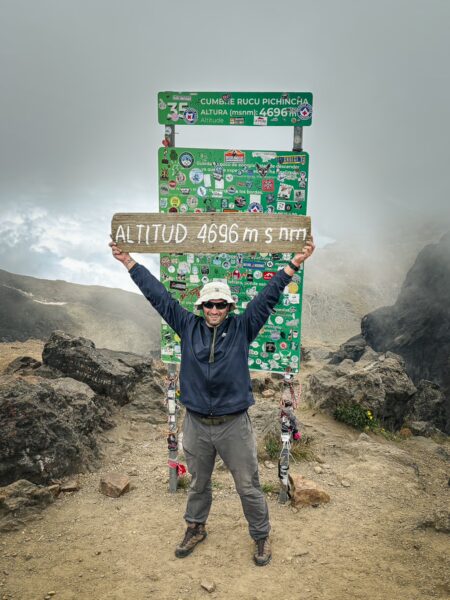Standing triumphantly at the 4695m altitude sign, a hiker enjoys the misty views atop Rucu Pichincha volcano in Ecuador.