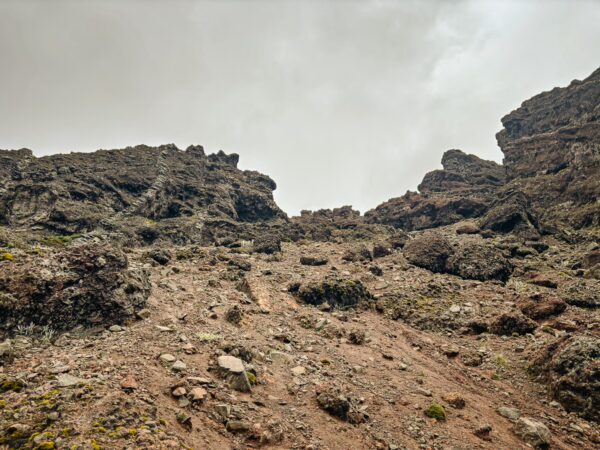 Steep rocky terrain of Volcán Ruminahui in Ecuador with rugged cliffs and a cloudy sky, showcasing natural geological features.