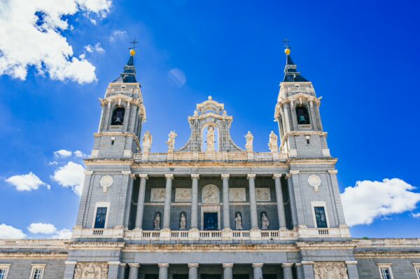 Stunning façade of Catedral de Santa María in Madrid, Spain, featuring intricate statues and twin towers against a bright blue sky.