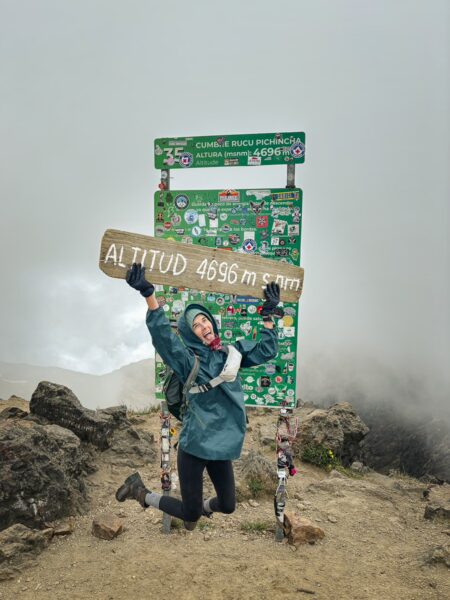 Joyful hiker posing with altitude sign at Rucu Pichincha Volcano, Ecuador, surrounded by mist and rocky terrain.