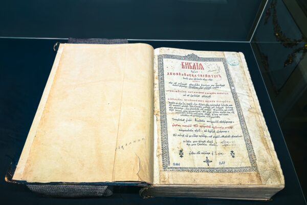 Old manuscript displayed at the art museum in Craiova, Romania, showcasing faded pages with elegant script and decorative borders.