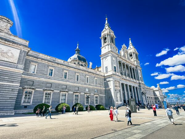 Catedral de Santa María in Madrid showcases striking architecture under a vibrant blue sky, bustling with visitors.