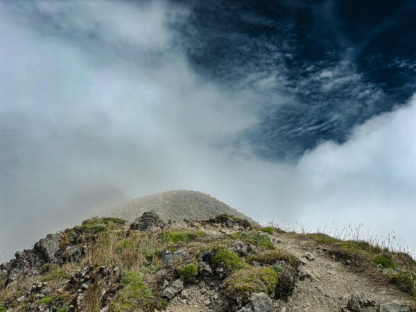 Majestic Imbabura Volcano rises above the clouds in Ecuador, showcasing rugged terrain and lush greenery against a dramatic sky.