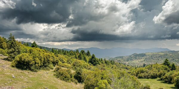 Lush green hills under a dramatic sky filled with dark clouds in Valtesiniko, Lagadia, Arcadia, Greece.