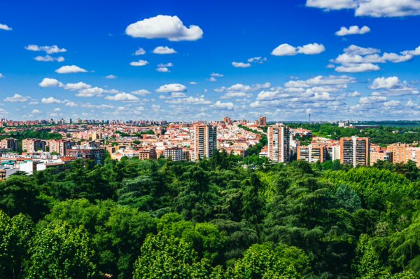 Lush greenery frames a vibrant cityscape under a bright blue sky with fluffy clouds, showcasing Madrid’s diverse architecture.
