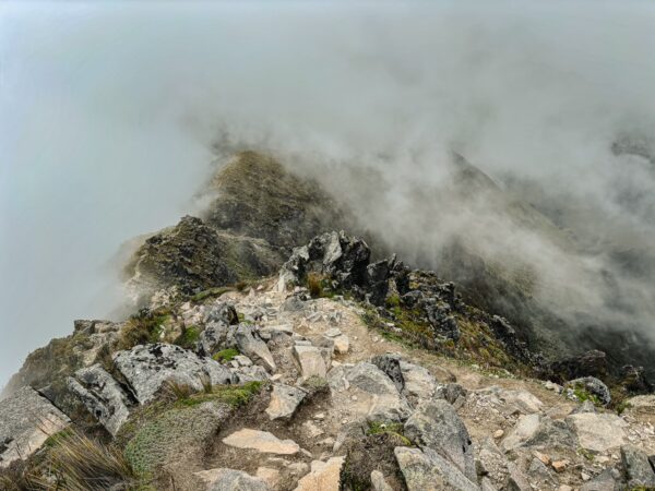 Stunning rocky cliffside with scattered boulders and misty clouds, overlooking the dramatic terrain of Imbabura Volcano, Ecuador.