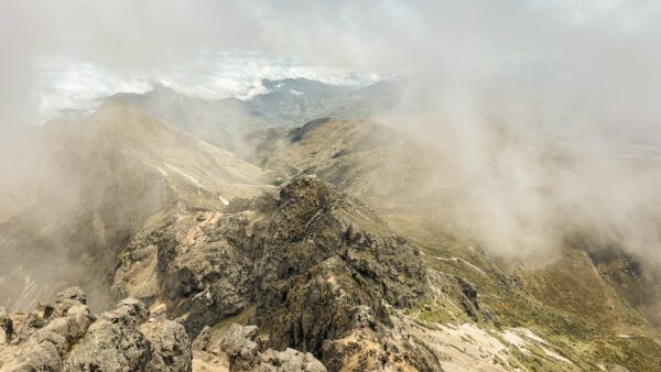 Breathtaking view from Rucu Pichincha Volcano, Ecuador, featuring rocky peaks shrouded in mist under a cloudy sky.