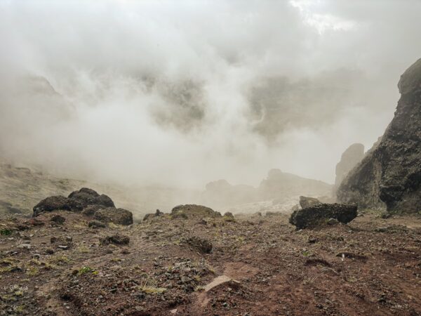 Fog envelops rugged terrain near Raminahui Volcano, Ecuador, with rocky outcrops emerging through the mist and soft earth tones.