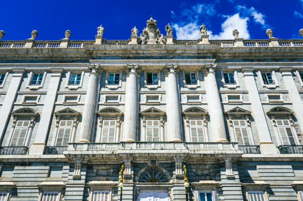Palacio Real features elegant columns and intricate sculptures under a vibrant blue sky in Madrid, Spain.