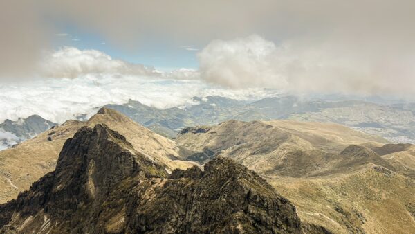 Stunning panoramic view from Rucu Pichincha Volcano, showcasing rugged peaks and a sea of clouds in Ecuador's mountainous landscape.