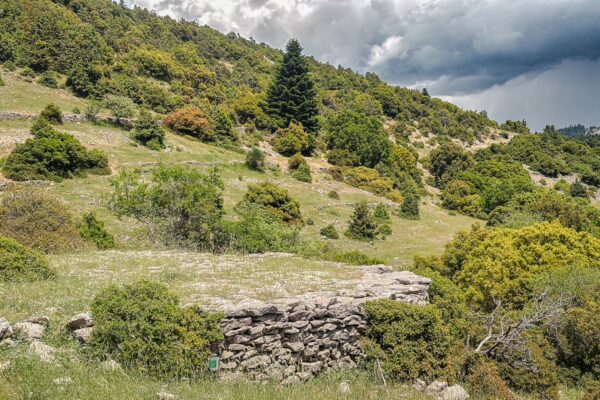 Stone wall amidst lush green hills under a cloudy sky in Valtesiniko, Lagadia, Arcadia, Greece.