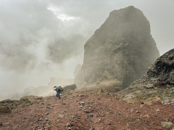 Hiker traversing rocky terrain amidst fog near Ruminahui Volcano, Ecuador, surrounded by dramatic cliffs and mist.