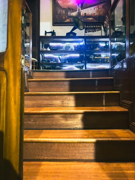 Wooden stairs lead up to a display showcasing artifacts and memorabilia, softly illuminated in a cozy Quito setting.