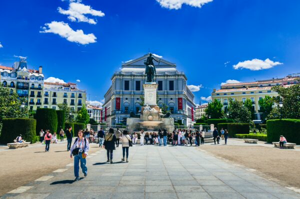 Visitors enjoy a sunny day at Plaza de Oriente in Madrid, surrounded by lush greenery and the grand Royal Theatre backdrop.