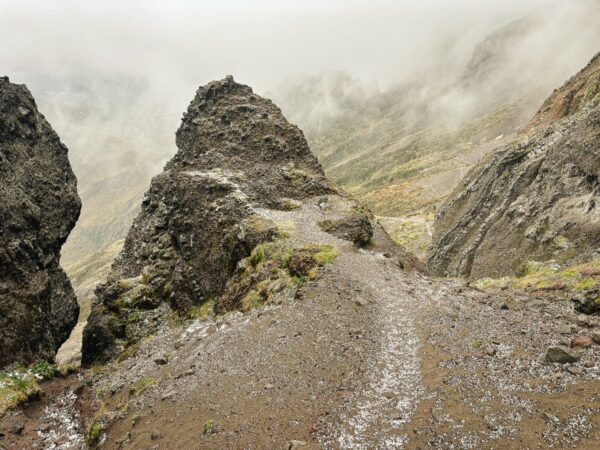 Rugged volcanic rock formations and a winding path surrounded by misty mountains near Raminahui, Ecuador.