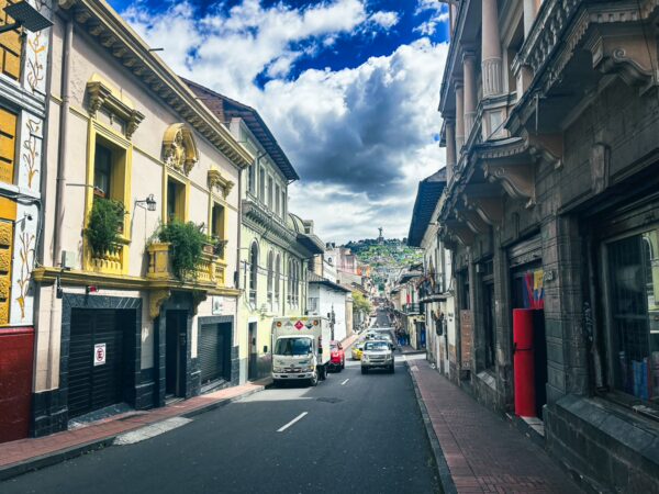 Charming streets of Quito showcase colorful colonial buildings and a scenic hillside in the background under a dramatic sky.
