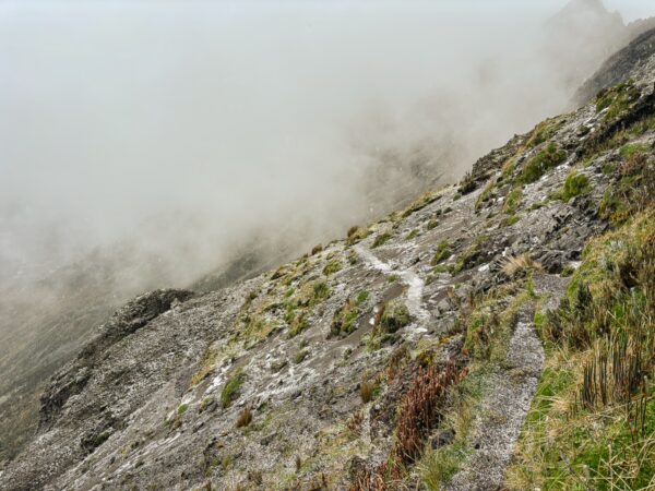 Lush green grasses and rocky terrain lead to the misty slopes of Volcán Ruminahui, Ecuador, creating an ethereal landscape.