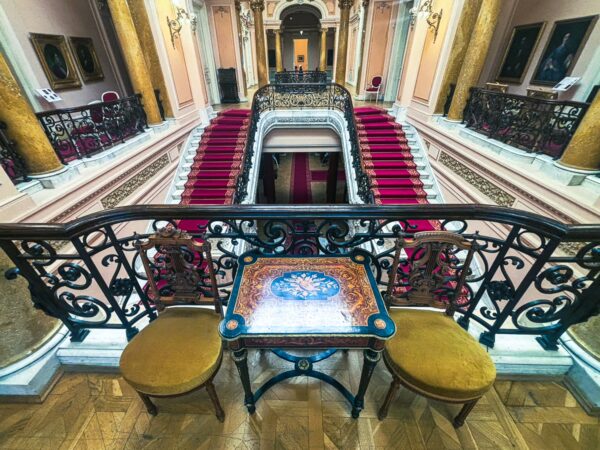 Elegant railing and ornate furnishings overlook a grand staircase with red carpet in the art museum, Craiova, Romania.
