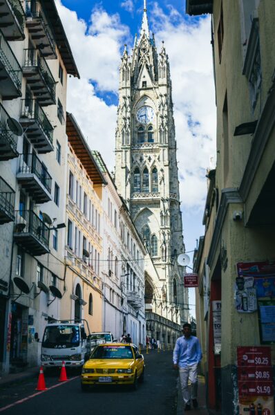Basilica del Voto Nacional towers over a narrow street in Quito, Ecuador, with a yellow taxi and clear blue skies overhead.