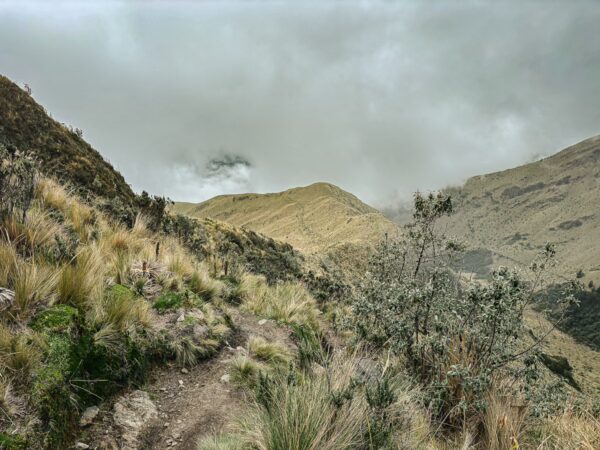 Majestic Imbabura Volcano rises above lush green hills and rugged trails under a cloudy sky in Ecuador.