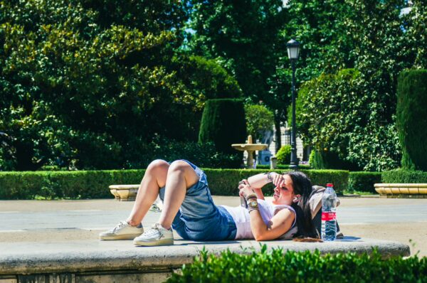 A woman relaxes on a stone ledge in Plaza de Oriente, Madrid, surrounded by lush greenery and a beautiful fountain.