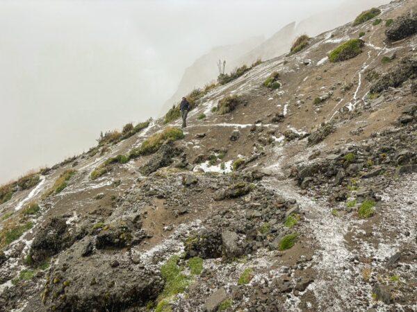 Fog blankets the rugged terrain of Ruminahui, with rocky paths and sparse vegetation visible along the mountainside.