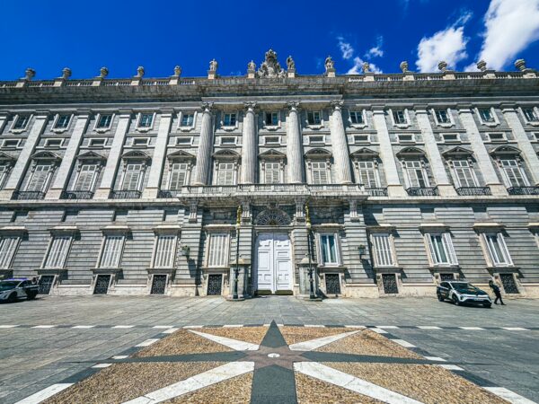 The grand façade of Palacio Real showcases intricate architectural details against a bright blue sky in Madrid, Spain.
