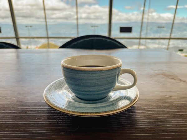A blue coffee cup on a saucer sits on a wooden table at the upper cable car station, overlooking the scenic Pichincha volcano in Ecuador.